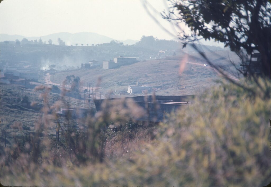 A obra vista de longe, através da vegetação, com a serra ao fundo — P0006 — Residência Luiz Carlos Bresser Pereira, Jardim Guedala — F016-P0006-1967-S03-D00009