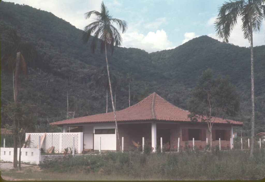Casa com telhado piramidal vista do gramado, entre coqueiros e morro de mata — P0007 — Residência Luiz França, Praia do Lázaro, Ubatuba — F016-P0007-1965-S03-D00017