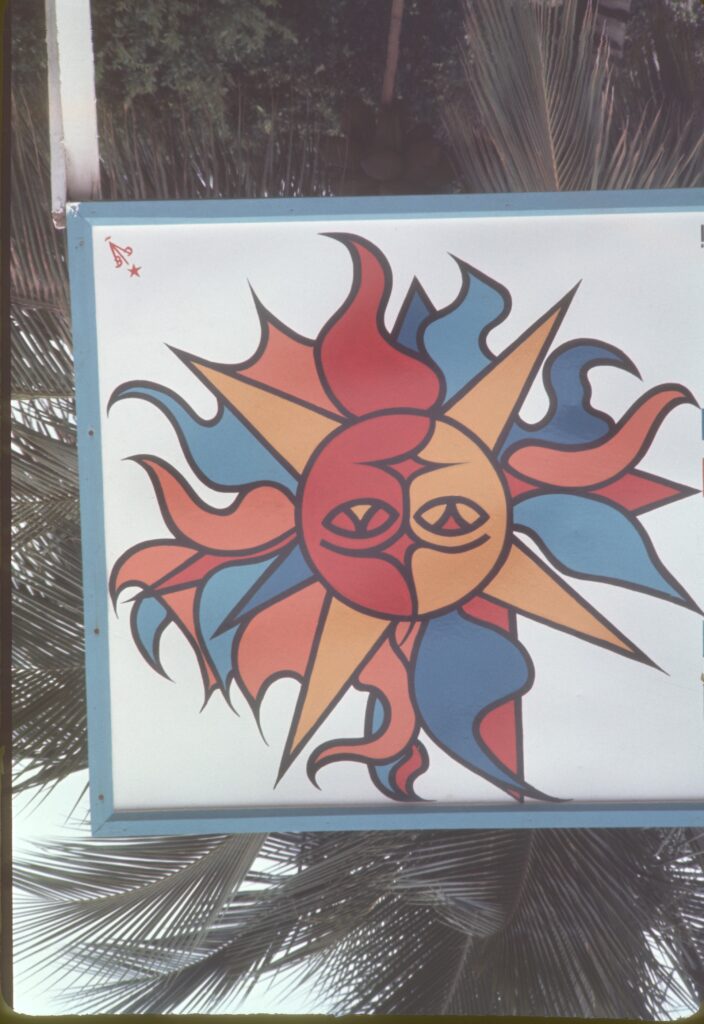 Placa pintada com um sol entre folhas de coqueiro — P0007 — Residência Luiz França, Praia do Lázaro, Ubatuba — F016-P0007-1965-S03-D00021