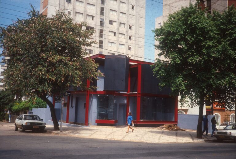 Edifício de esquina com estrutura vermelha (obra não identificada)