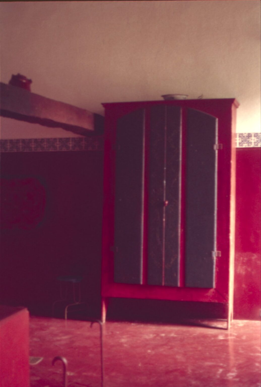 Armário de madeira com portas escuras em ambiente interno, foto com forte dominante de cor avermelhada — P0024 — Fazenda Fernando Millan — F016-P0024-1981-S03-D00020