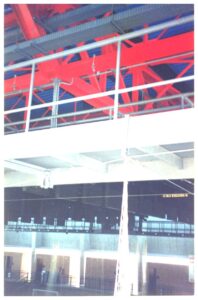 Detalhe da estrutura metálica interna de um pavilhão, com vigas vermelhas e rede suspensa ao fundo — P0131 — SESC - Piracicaba
