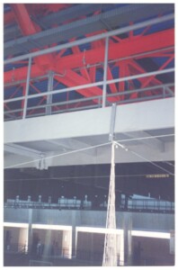 Detalhe da estrutura metálica interna de um pavilhão, com vigas vermelhas e rede suspensa ao fundo — P0131 — SESC - Piracicaba