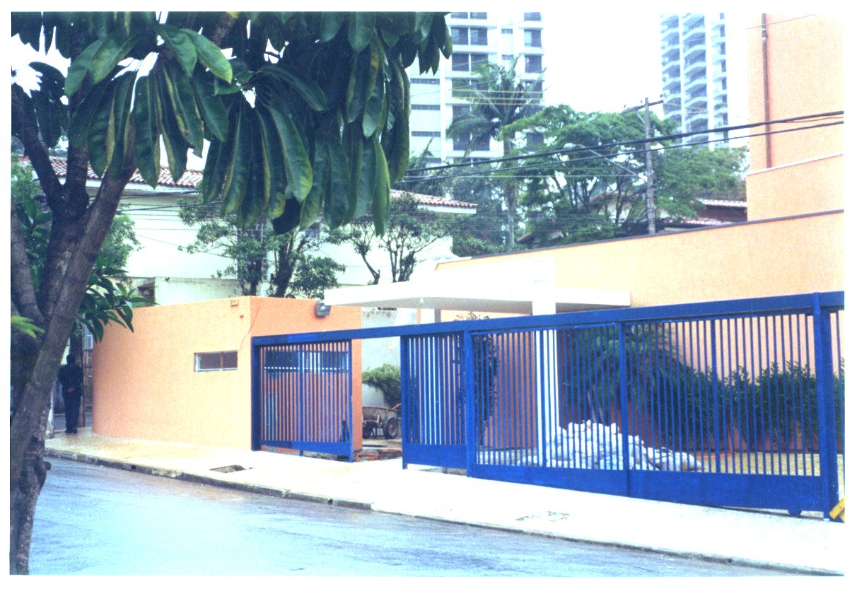 Fachada e portão de acesso de edificação em esquina, com muro na cor laranja e grade metálica azul, vista a partir da calçada — P0131 — SESC - Piracicaba — F009-P0131-0000-S03-D00038