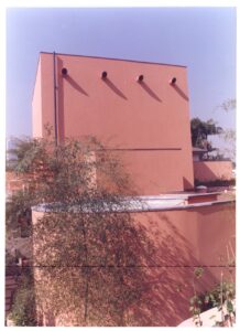 Fachada em tom terracota com quatro aberturas circulares na base e cobertura translúcida ao fundo, parcialmente obstruída por árvore — P0131 — SESC - Piracicaba