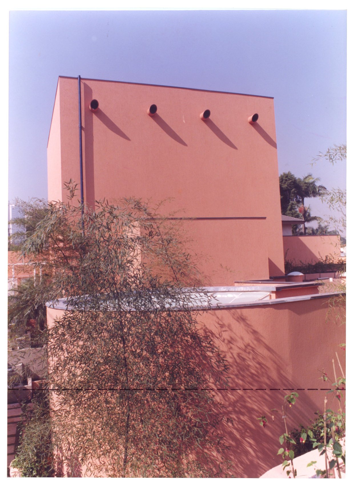 Fachada em tom terracota com quatro aberturas circulares na base e cobertura translúcida ao fundo, parcialmente obstruída por árvore — P0131 — SESC - Piracicaba — F009-P0131-0000-S03-D00014