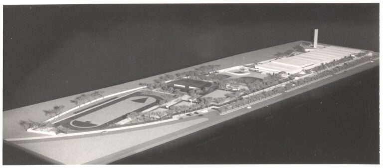 Maquete de projeto urbanístico mostrando pista de atletismo, área verde, edificações baixas e uma torre/chaminé