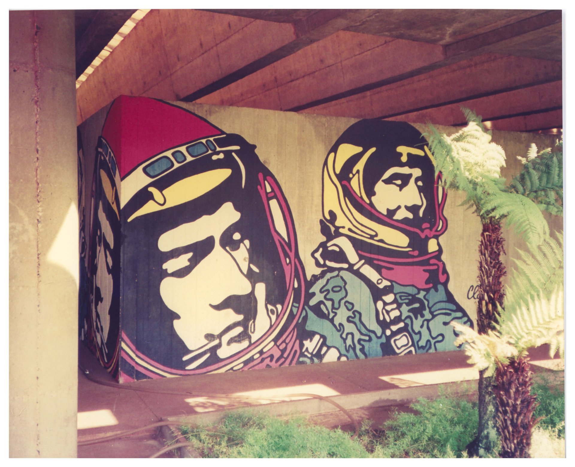 Mural com figuras estilizadas de astronautas pintado em pilar de concreto sob viaduto, cercado por vegetação — P0015 — SESI — Ribeirão Preto — F009-P0015-1973-S03-D00031