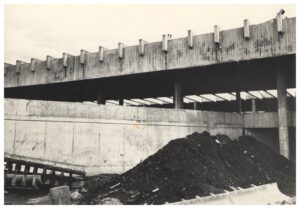 Obra em andamento: estrutura de concreto armado com vigas em balanço e muro de contenção, com monte de terra e entulho em primeiro plano — P0015 — SESI — Ribeirão Preto