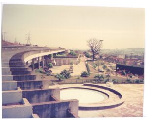 Vista a partir de arquibancada de concreto, mostrando terraço circular com espelho d'água, jardins ajardinados e paisagem urbana ao fundo — P0015 — SESI — Ribeirão Preto