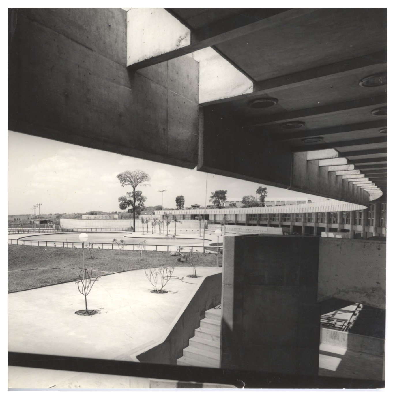 Vista a partir de marquise em concreto mostrando pátio, escadaria e edificação curva ao fundo com jardim circular — P0015 — SESI — Ribeirão Preto — F009-P0015-1973-S03-D00009