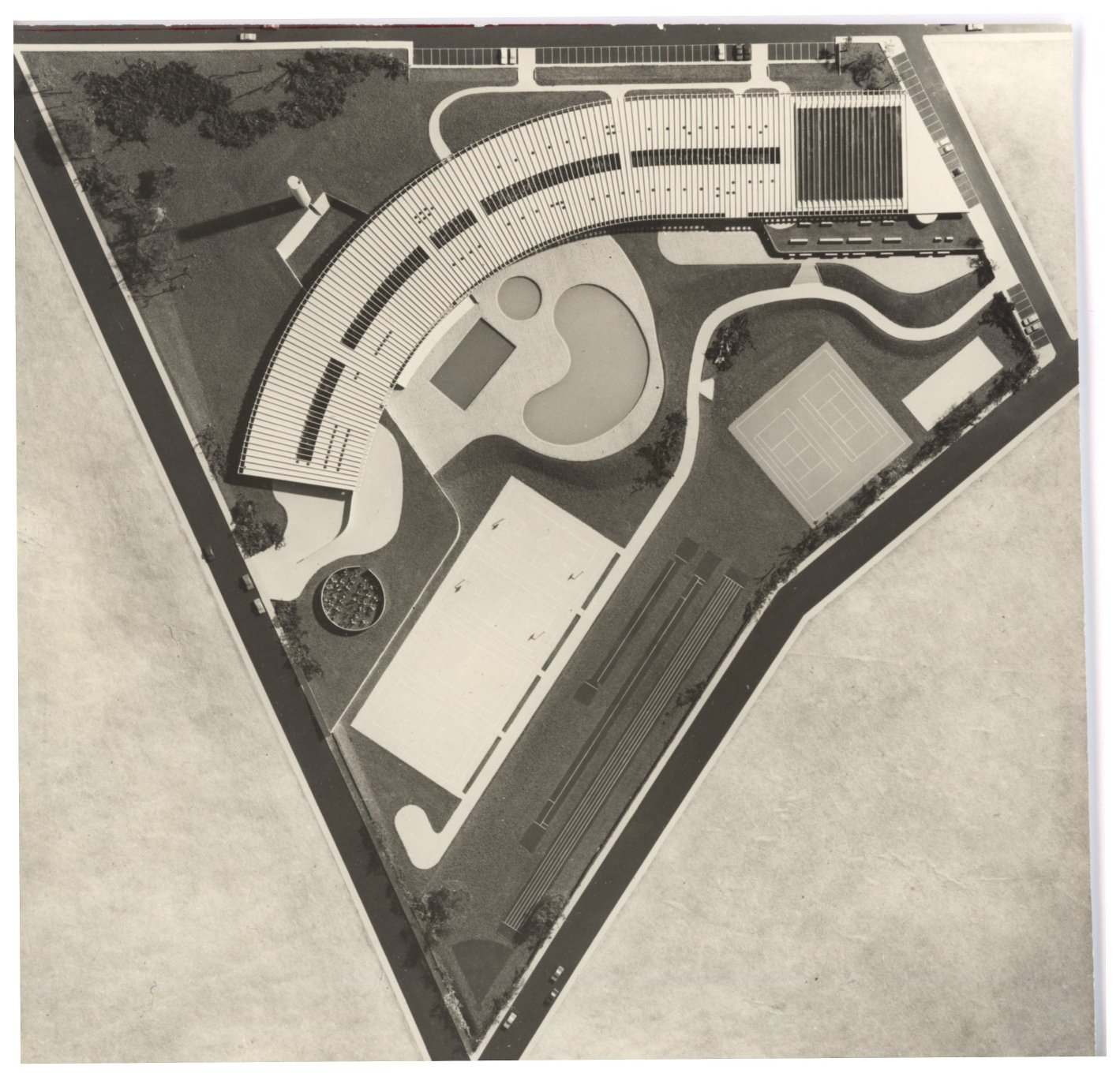 Vista aérea de conjunto arquitetônico com edifício curvo, piscina em formato irregular, quadras esportivas e áreas verdes, delimitado por via em formato triangular — P0015 — SESI — Ribeirão Preto — F009-P0015-1973-S03-D00013