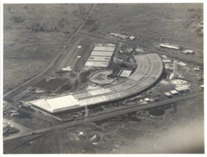 Vista aérea de edifício em construção com cobertura curva em forma de ferradura, rodeado por área rural e estrada — P0015 — SESI — Ribeirão Preto