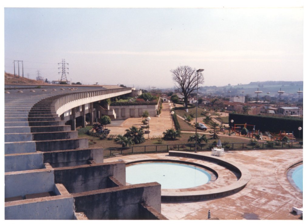 Vista aérea parcial de edifício com marquise curva em concreto, jardins, piscina circular e área de lazer, com a cidade ao fundo — P0015 — SESI — Ribeirão Preto — F009-P0015-1973-S03-D00055