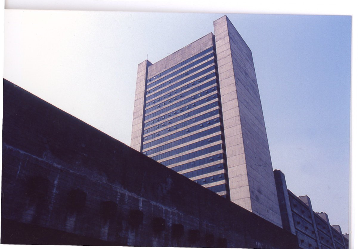 Vista ascendente de edifício alto de concreto com fachada em faixas horizontais de janelas, fotografado a partir de uma estrutura em sombra em primeiro plano — P0018 — Correios — Sede Regional e Centro de Triagem — F009-P0018-1975-S03-D00022