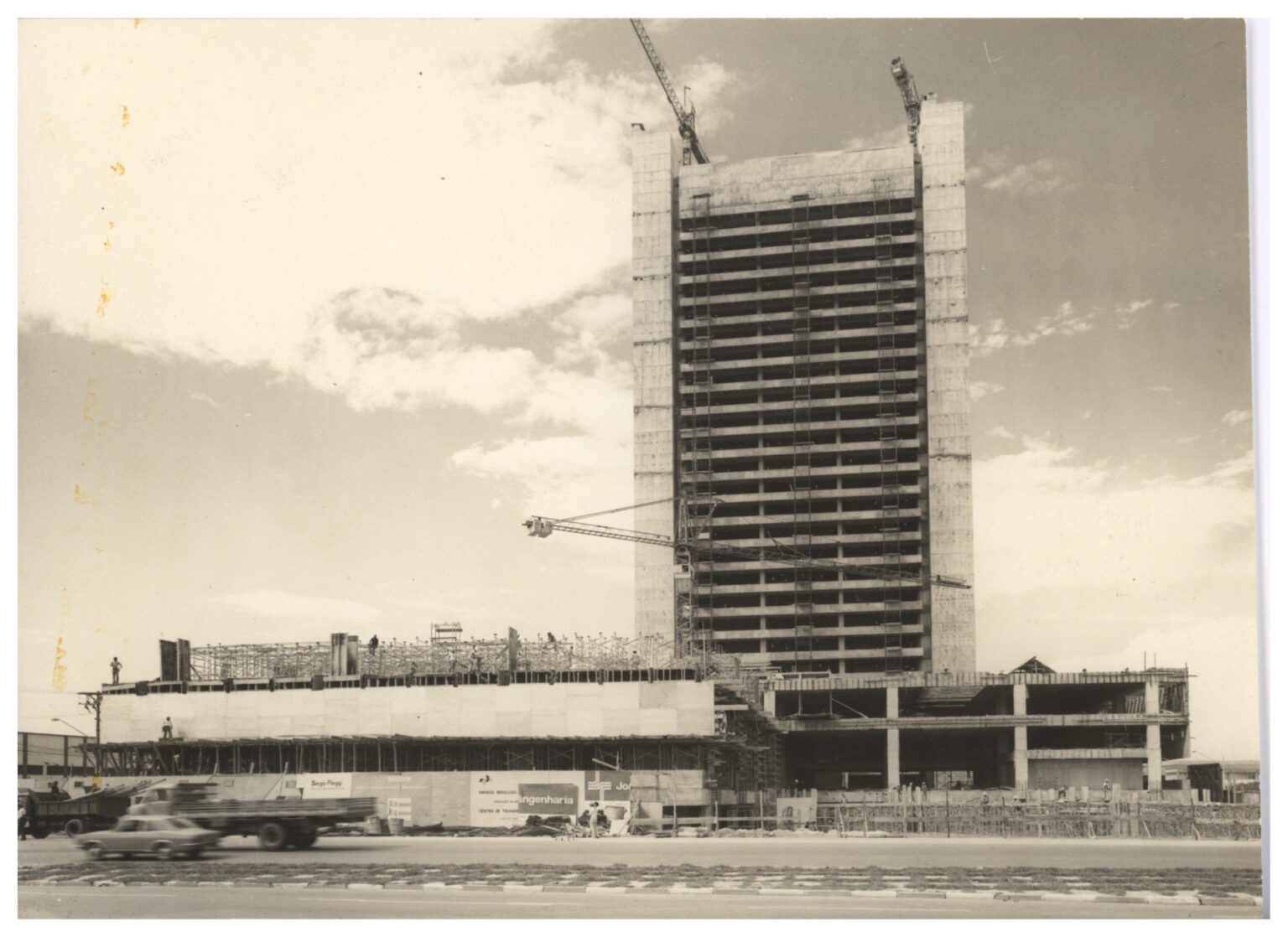 Vista de construção de edifício alto, com estrutura de concreto aparente e guindastes, céu nublado ao fundo — P0018 — Correios — Sede Regional e Centro de Triagem — F009-P0018-1975-S03-D00001