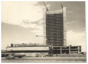 Vista de construção de edifício alto, com estrutura de concreto aparente e guindastes, céu nublado ao fundo — P0018 — Correios — Sede Regional e Centro de Triagem