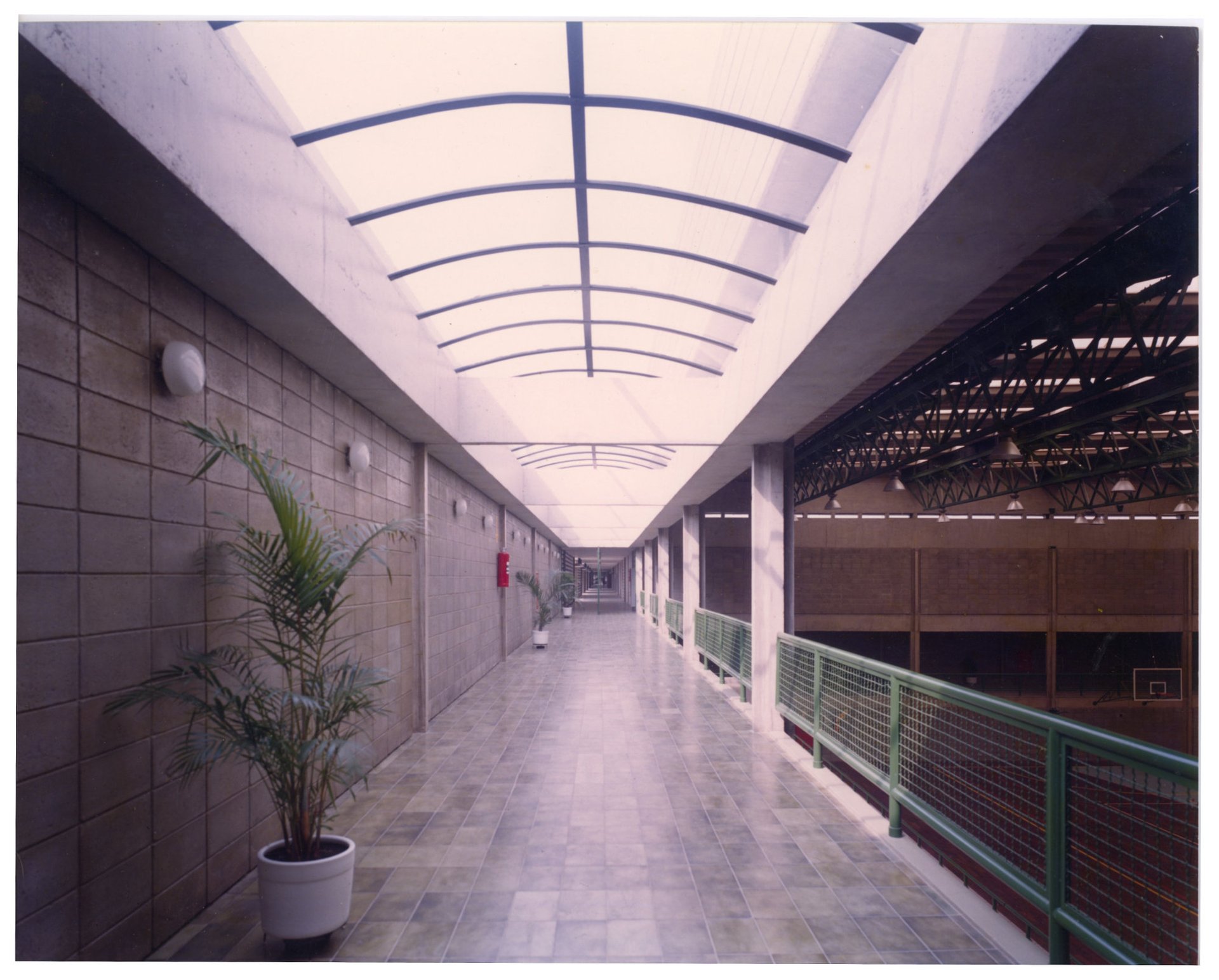 Vista de corredor interno com piso decorado em padrão de arcos, estrutura metálica verde à esquerda e parede de blocos de concreto à direita — P0055 — SESI — São José dos Campos — F009-P0055-1979-S03-D00006