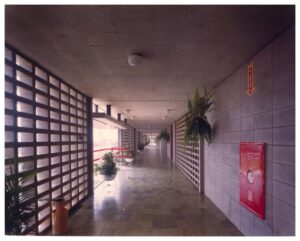 Vista de corredor interno com piso em grelha, plantas suspensas e placa de extintor/sinalização de rota de fuga — P0055 — SESI — São José dos Campos