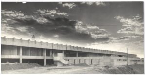 Vista de edifício em obras, com estrutura de concreto aparente, pilares e vigas, terreno ao fundo e céu com nuvens (imagem invertida) — P0015 — SESI — Ribeirão Preto