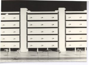 Vista de maquete arquitetônica mostrando fachada com elementos horizontais sobrepostos (possíveis brises ou lajes) e pilares verticais, com vegetação suspensa na parte superior — P0018 — Correios — Sede Regional e Centro de Triagem