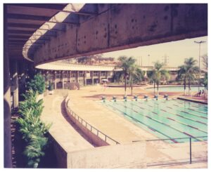 Vista de piscina com raias demarcadas, blocos de partida e arquibancada curva de concreto, com vegetação ao fundo — P0015 — SESI — Ribeirão Preto