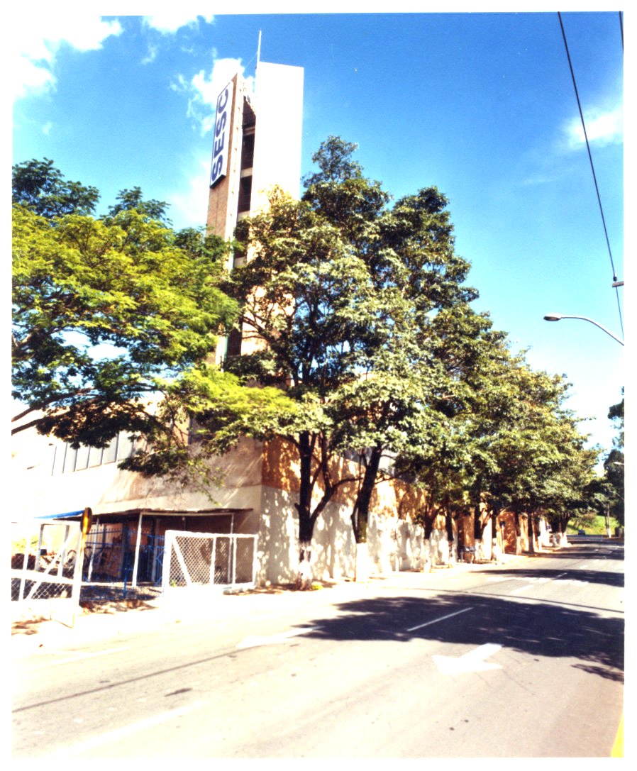 Vista de rua com edifício de torre vertical e letreiro, avenida arborizada em primeiro plano — P0131 — SESC - Piracicaba — F009-P0131-0000-S03-D00027
