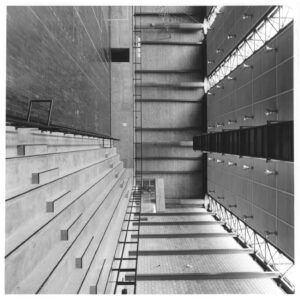 Vista de um pátio ou área entre construções, mostrando arquibancada em concreto à esquerda e fachada com luminárias à direita; imagem registrada em ângulo rotacionado — P0060 — SESI — Marília