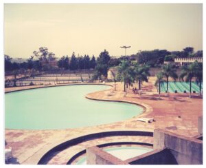 Vista elevada de complexo esportivo com piscina de formato orgânico, piscina de raias, quadras ao fundo e área de piscina circular em primeiro plano — P0015 — SESI — Ribeirão Preto