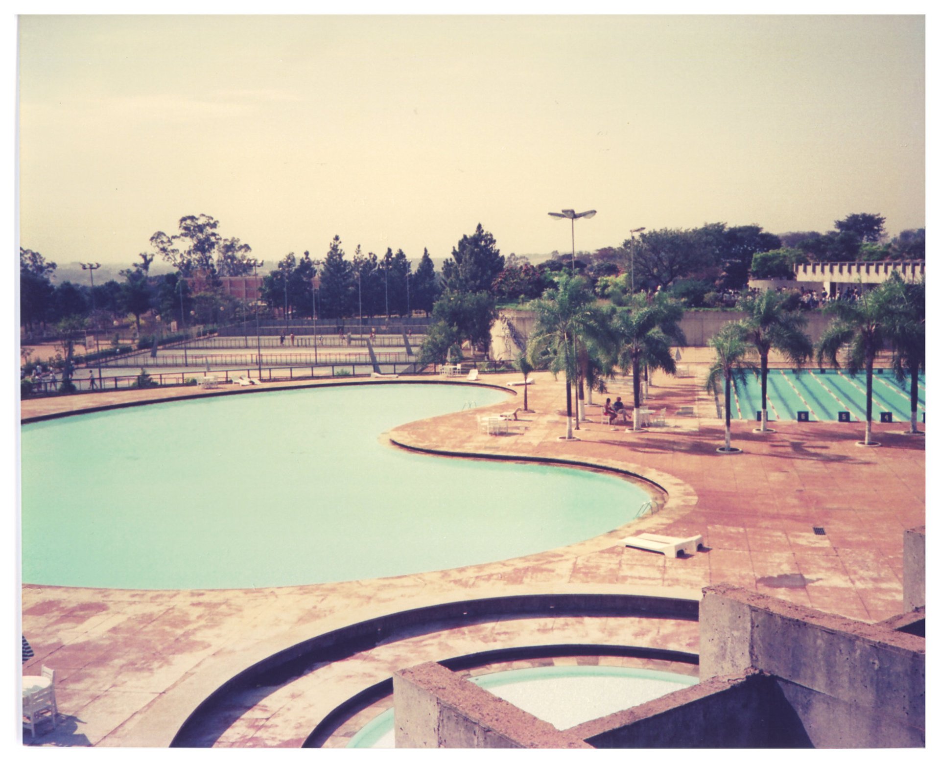Vista elevada de complexo esportivo com piscina de formato orgânico, piscina de raias, quadras ao fundo e área de piscina circular em primeiro plano — P0015 — SESI — Ribeirão Preto — F009-P0015-1973-S03-D00025