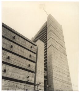 Vista em perspectiva ascendente de edifício de concreto aparente, destacando o volume vertical da torre e o painel de brises laterais — P0018 — Correios — Sede Regional e Centro de Triagem