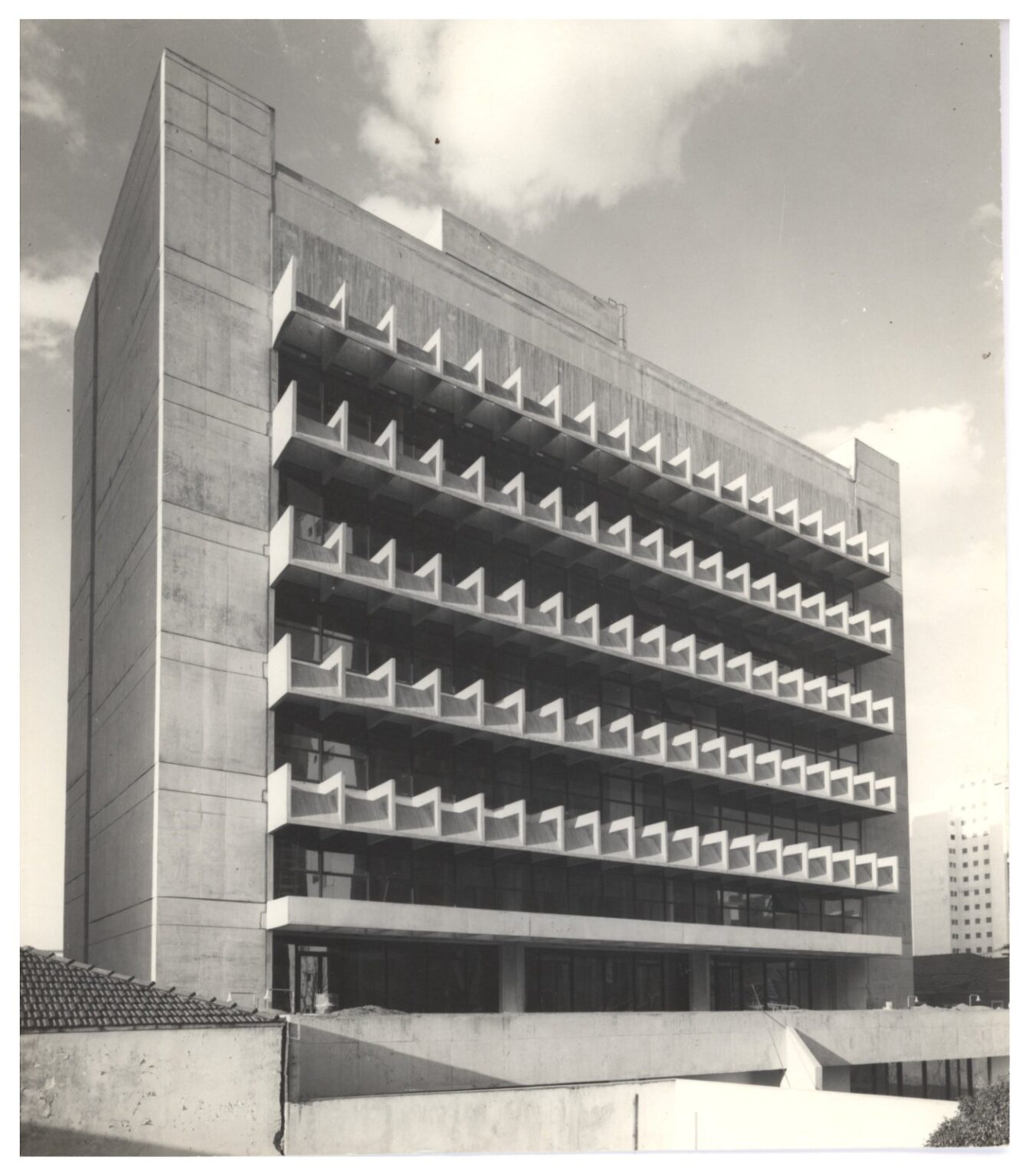 Vista em perspectiva de edifício modernista de múltiplos pavimentos, destacando fachada com elementos de proteção solar (brises) em concreto aparente, dispostos em padrão geométrico repetitivo — P0112 — SENAC — Av. Francisco Matarazzo — F009-P0112-1972-S03-D00007