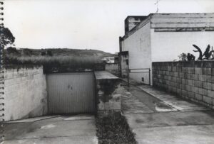 Vista externa de casa mostrando portão de garagem, muro, calçada e número de identificação "162" no portão lateral — P0001 — Residência Teresa Martino