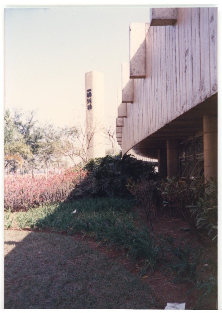 Vista externa de edifício com cobertura/marquise em concreto, coluna com numeração, cercado por árvores e jardim — P0015 — SESI — Ribeirão Preto — F009-P0015-1973-S03-D00036