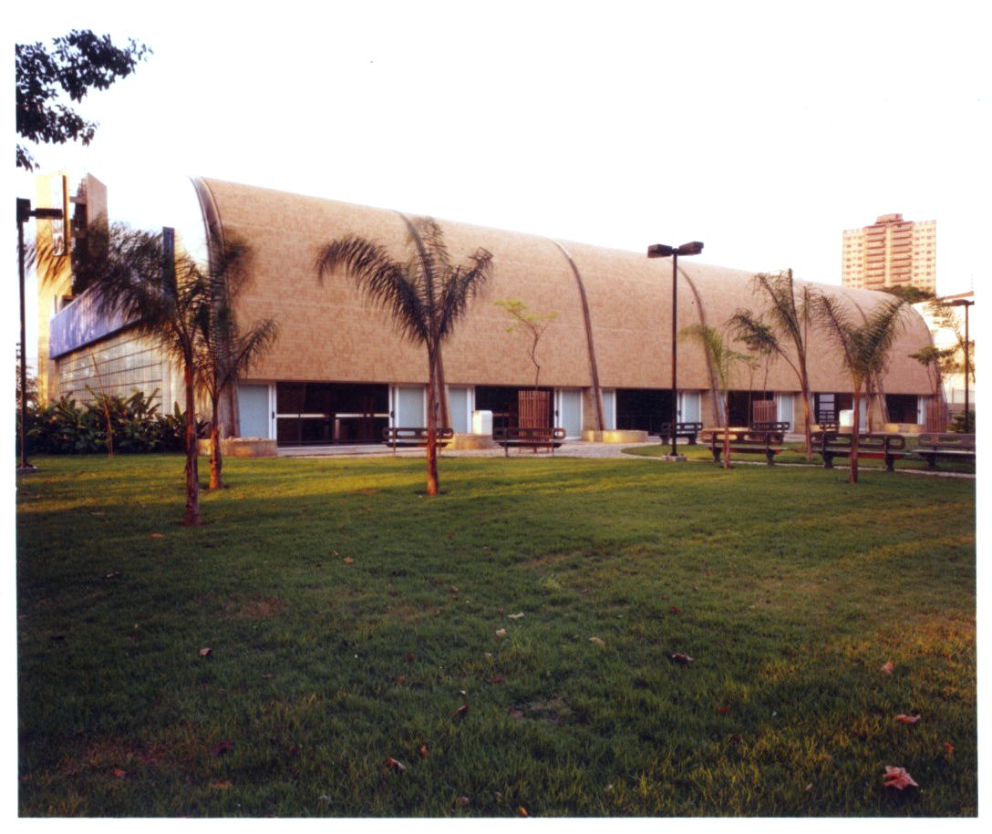Vista externa de edifício com fachada curva, cercado por gramado, árvores e postes de iluminação — P0131 — SESC - Piracicaba — F009-P0131-0000-S03-D00033