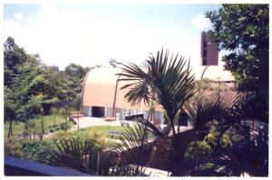 Vista externa de edifício com pátio, gramado e vegetação ao redor — P0131 — SESC - Piracicaba