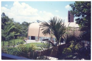 Vista externa de edifício com pátio, gramado e vegetação ao redor — P0131 — SESC - Piracicaba