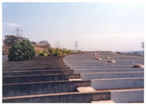 Vista externa de edifício com volumes escalonados em concreto aparente, com torres de energia e vegetação ao fundo — P0015 — SESI — Ribeirão Preto