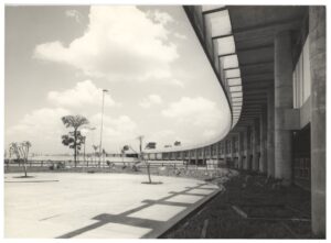 Vista externa de edifício de arquitetura moderna com fachada curva em brises de concreto e pilotis, com jardim e árvores em primeiro plano — P0015 — SESI — Ribeirão Preto