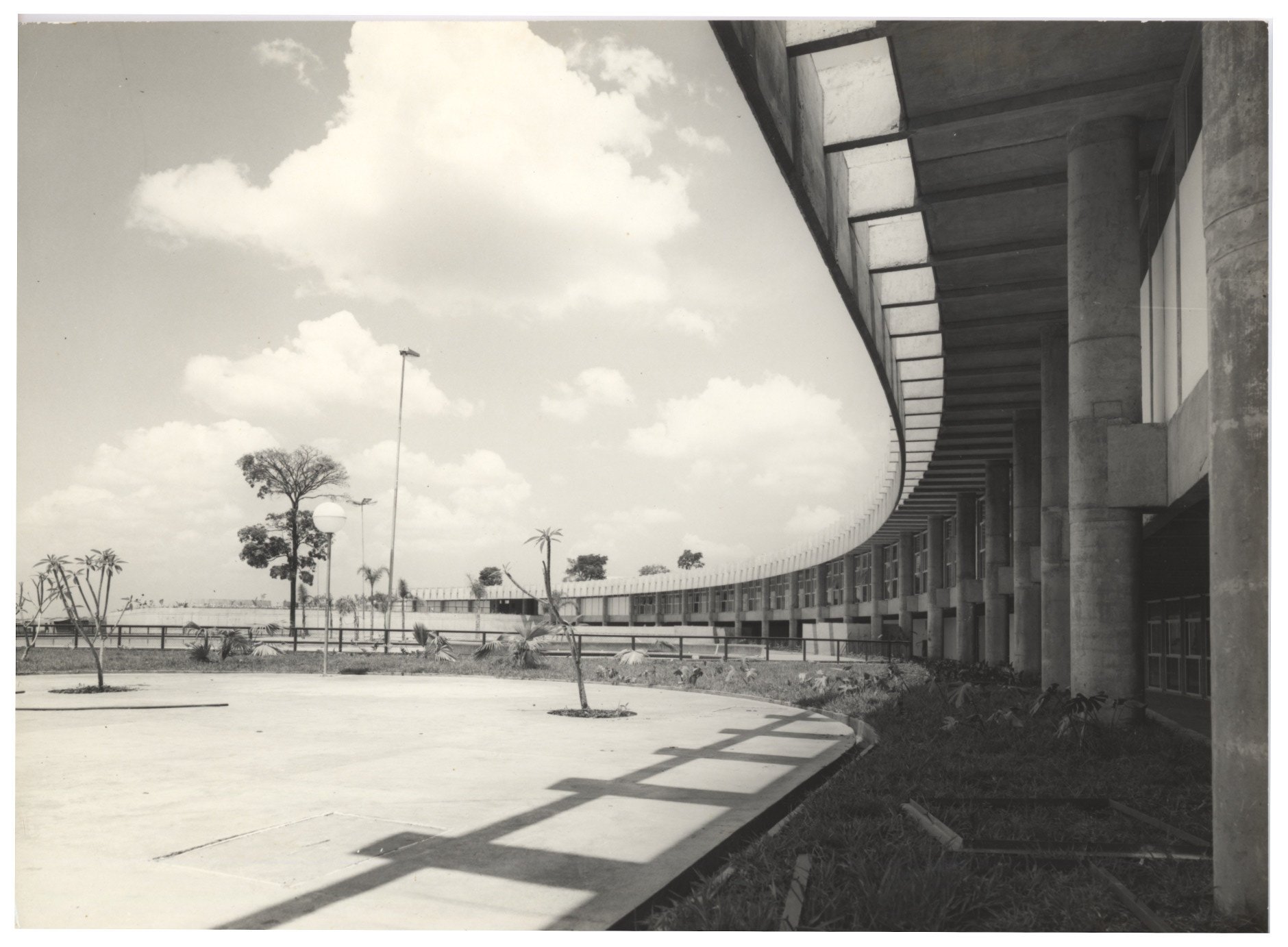 Vista externa de edifício de arquitetura moderna com fachada curva em brises de concreto e pilotis, com jardim e árvores em primeiro plano — P0015 — SESI — Ribeirão Preto — F009-P0015-1973-S03-D00012