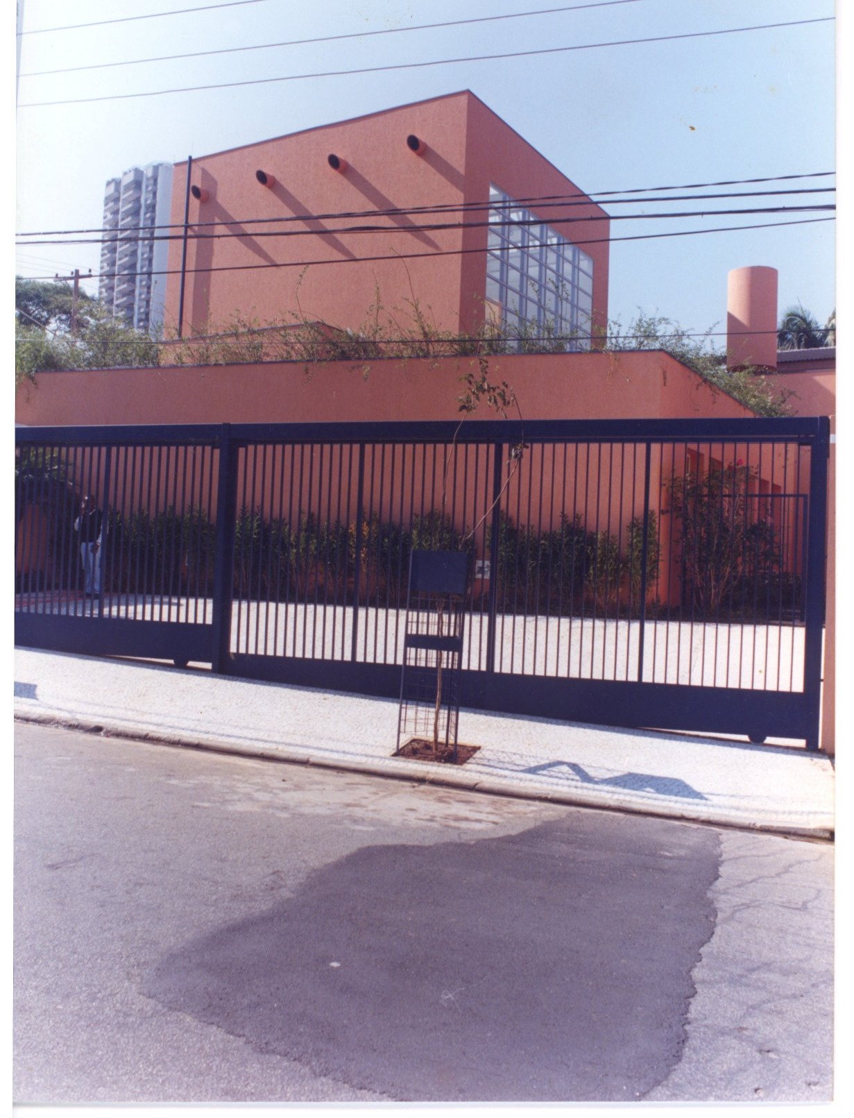 Vista externa de edifício em tom terracota, com grade metálica, árvores e calçada em primeiro plano — P0131 — SESC - Piracicaba — F009-P0131-0000-S03-D00009