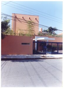 Vista externa de fachada residencial com muro de grade azul, volume terracota e marquise em balanço — P0131 — SESC - Piracicaba