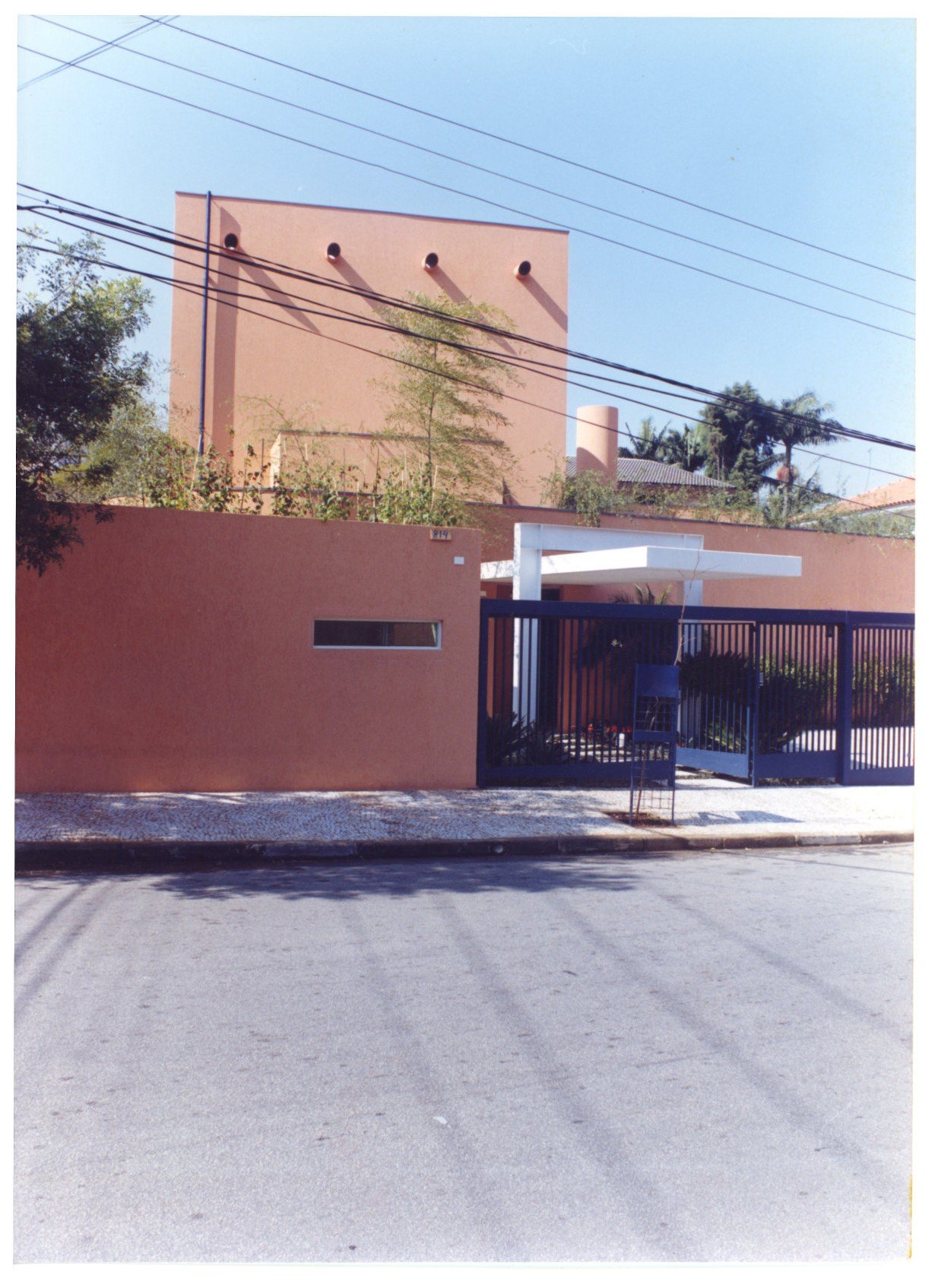 Vista externa de fachada residencial com muro de grade azul, volume terracota e marquise em balanço — P0131 — SESC - Piracicaba — F009-P0131-0000-S03-D00012