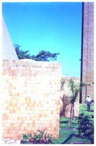 Vista externa de telhado de telhas cerâmicas e parede de tijolos, com árvore e pessoa ao fundo — P0131 — SESC - Piracicaba