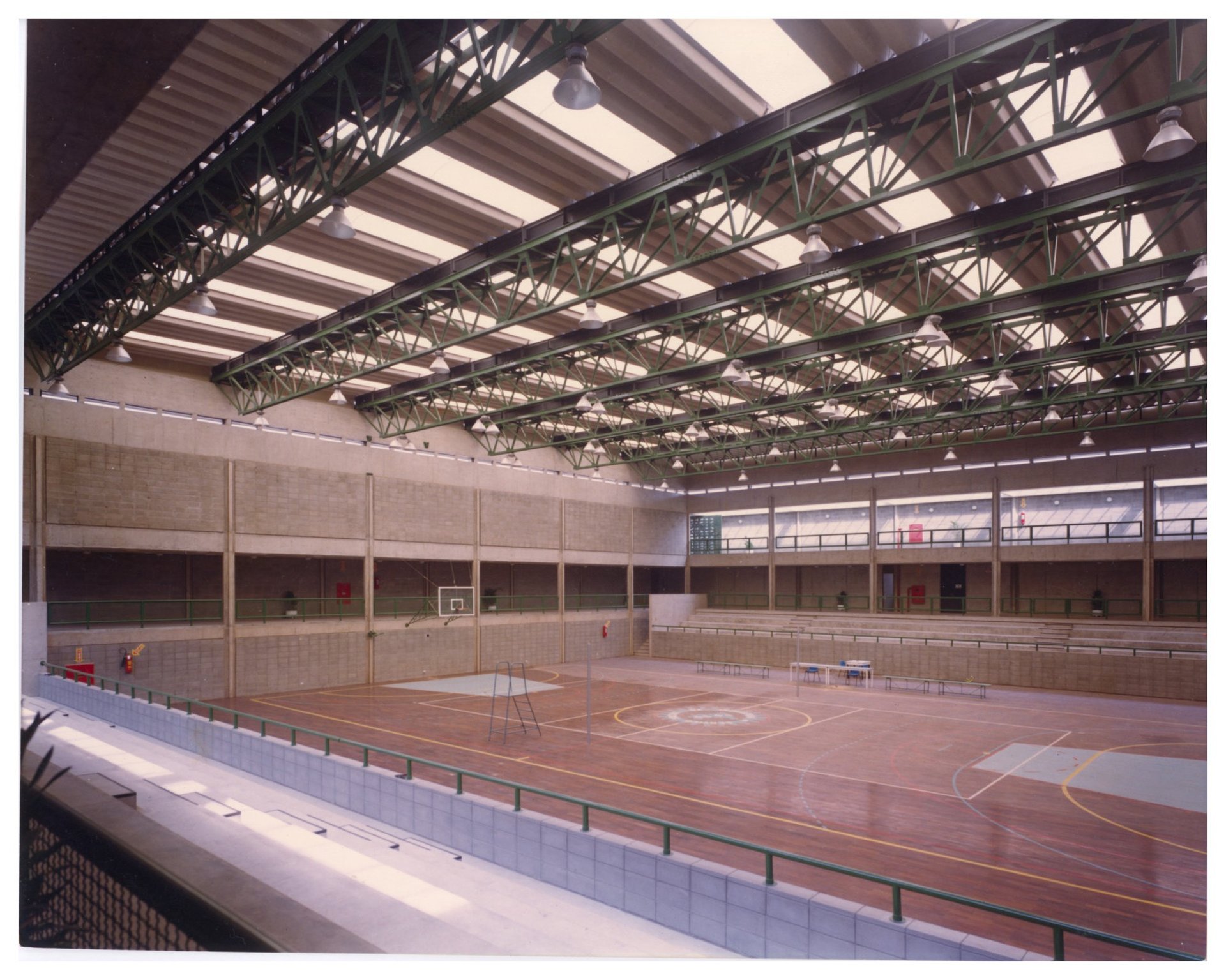 Vista interior de pavilhão desportivo coberto, com pista de madeira marcada e estrutura reticulada metálica de suporte da cobertura — P0055 — SESI — São José dos Campos — F009-P0055-1979-S03-D00013