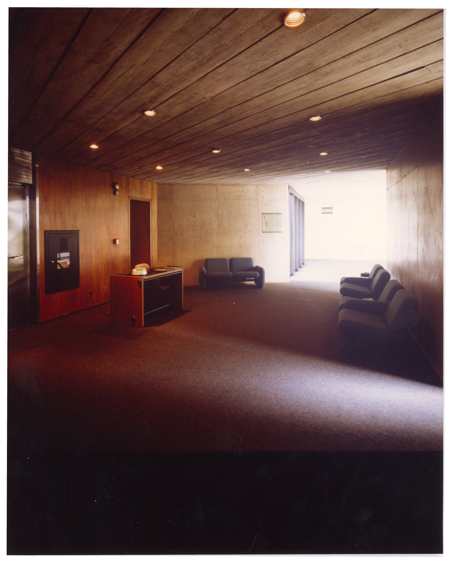 Vista interna de ambiente revestido em madeira com poltronas estofadas, móvel baixo e pontos de luz embutidos na parede — P0019 — Salles Publicidade — São Paulo — F009-P0019-1977-S03-D00007