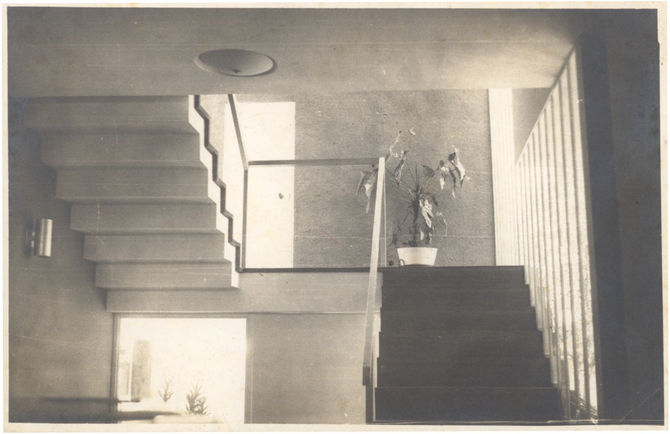 Vista interna de escada com degraus em balanço, guarda-corpo de vidro e teto com ripas, em ambiente de arquitetura modernista — P0001 — Residência Aecio Aeouche de Toledo — F004-P0001-1960-S03-D00004