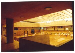 Vista interna de ginásio esportivo em concreto aparente, com quadra de basquete, arquibancadas e grupo de pessoas praticando esporte — P0015 — SESI — Ribeirão Preto