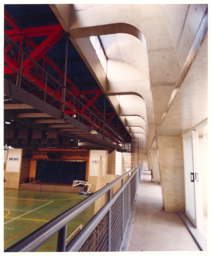 Vista interna de ginásio esportivo, mostrando estrutura metálica e elementos de concreto, com quadra ao fundo e placas identificadas como 'SESC — P0131 — SESC - Piracicaba — F009-P0131-0000-S03-D00023