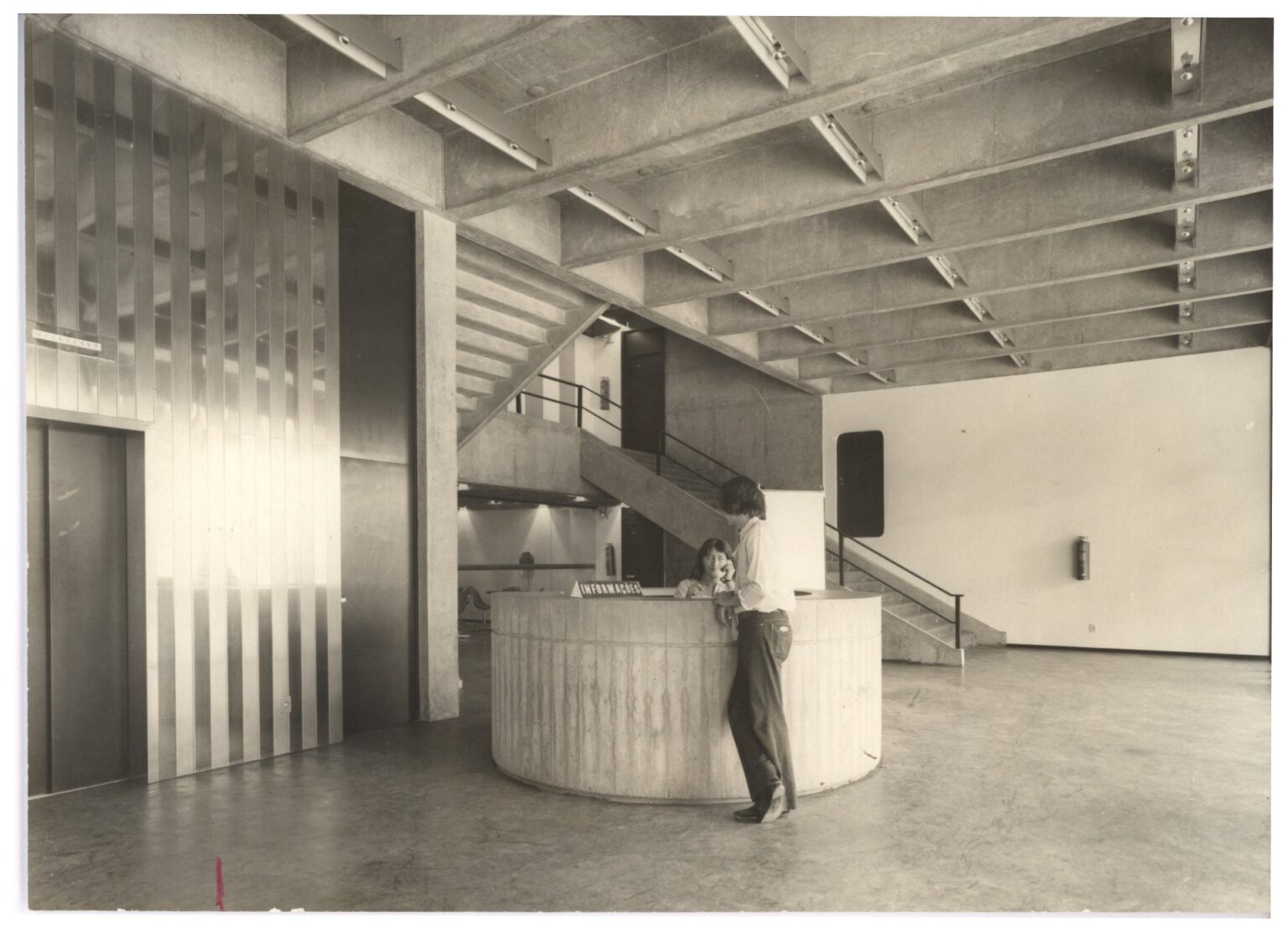 Vista interna de hall de edifício com balcão de "Informações" em formato cilíndrico, estrutura de concreto ripada e pessoas conversando junto ao balcão — P0112 — SENAC — Av. Francisco Matarazzo — F009-P0112-1972-S03-D00015